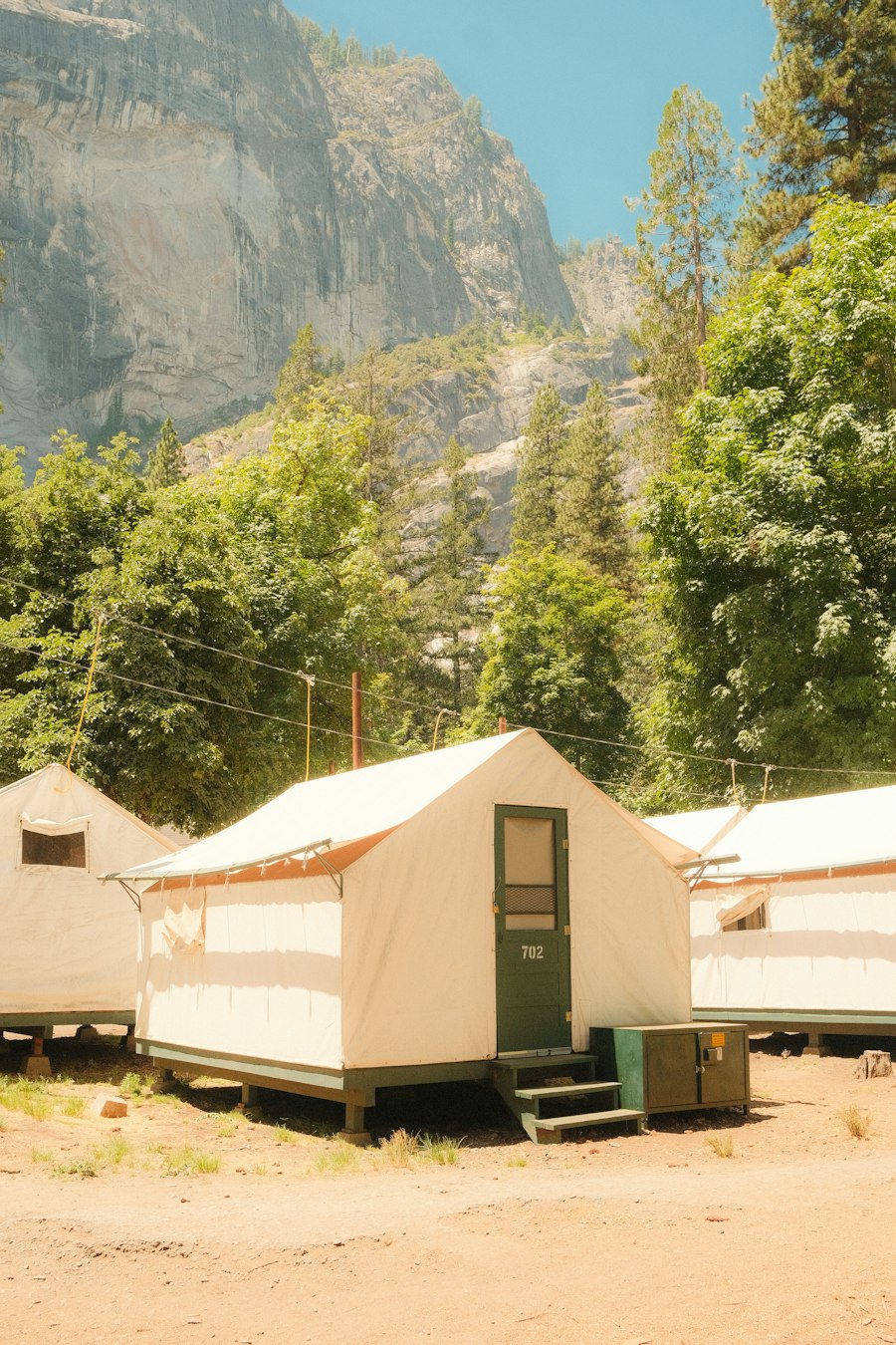 A row of white canvas tent cabins beneath trees and a rocky hillside